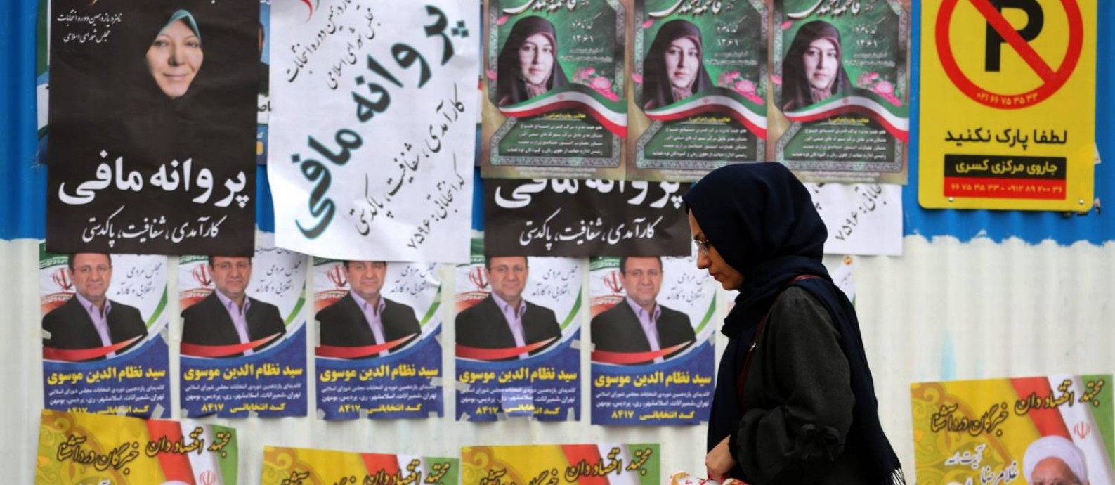 Iraniana passa por cartazes de candidatos no último dia de campanha em Teerã Foto: ATTA KENARE / ATTA KENARE/AFP