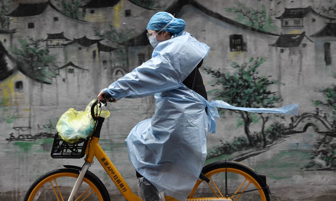 Mullher usando equipamento de proteção anda de bicicleta em Wuhan, cidade chinesa epicentro da epidemia Foto: STRINGER / REUTERS