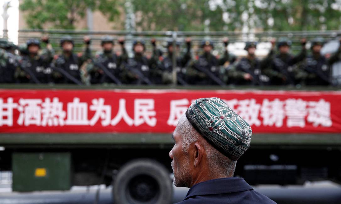 Membros da minoria muçulmana uigur diante de comboi paramilitar na região Xinjiang Foto: Reuters