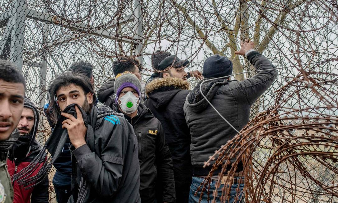 Imigrantes tentam cortar cerca de arame farpado para fugir da polícia grega Foto: BULENT KILIC / AFP