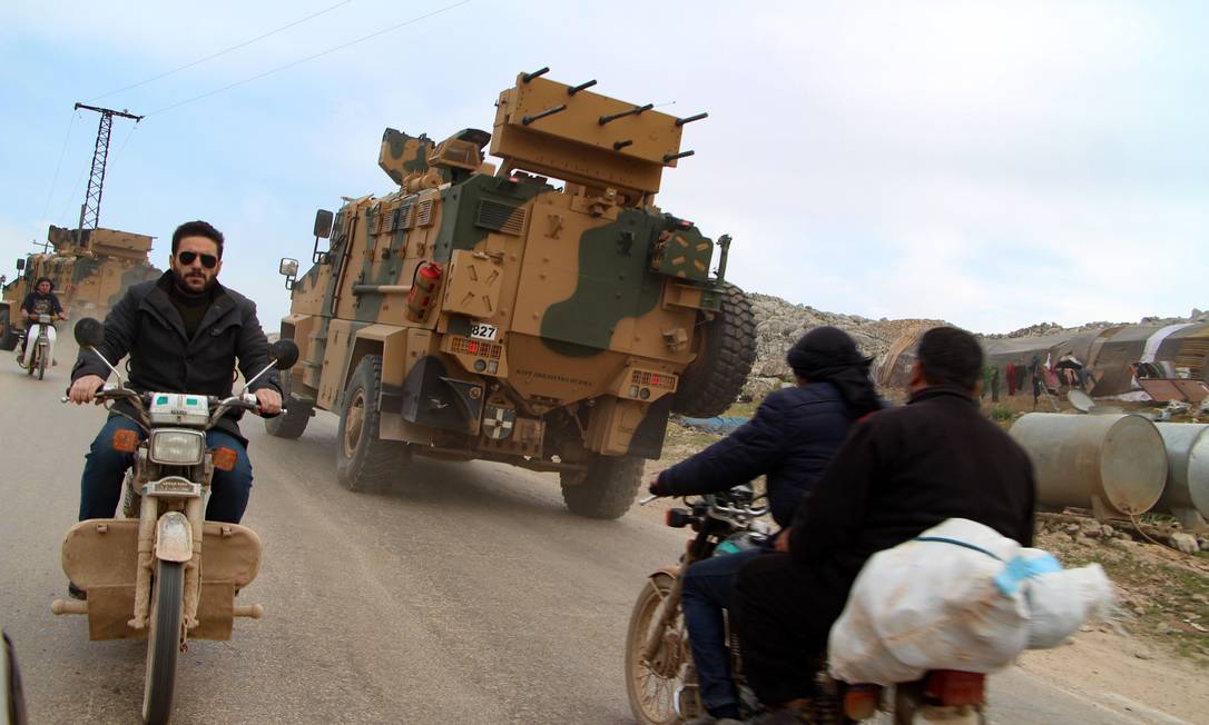 Motos trafegam ao lado de veículos militares turcos perto da vila de Kafr Lusin, na província síria de Idlib, horas depois do início do cessar-fogo na região Foto: IBRAHIM YASOUF / AFP
