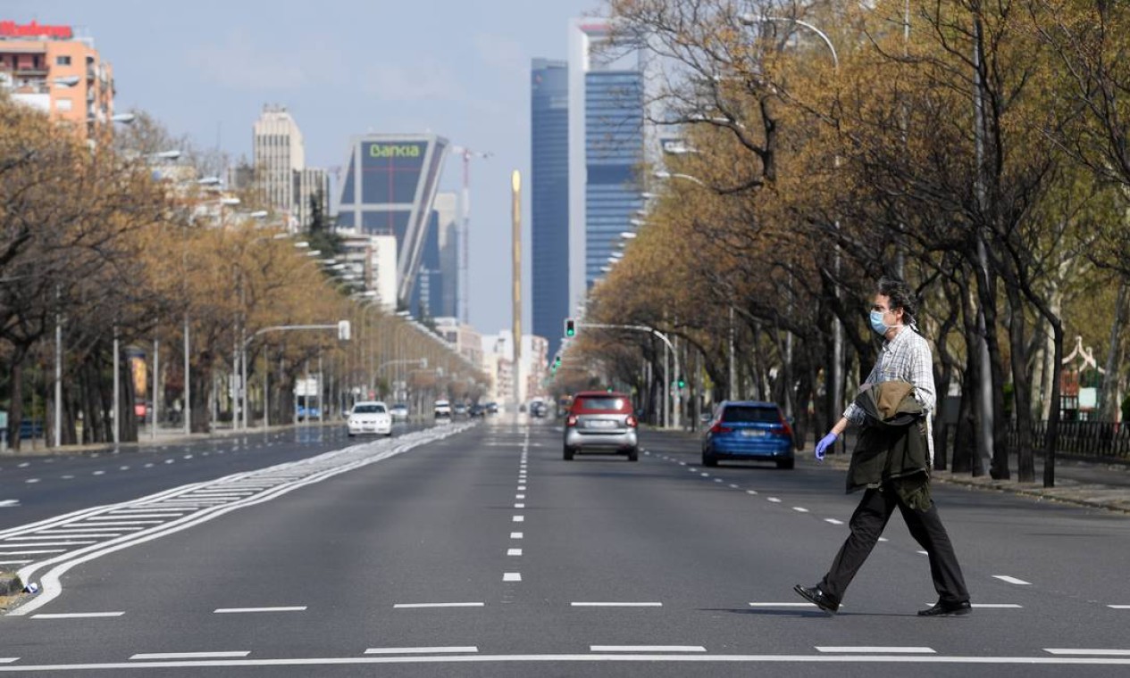 Homem de máscara e luvas atravessa a avenida La Castellana, em Madri, quase deserta Foto: Oscar del Pozo / AFP