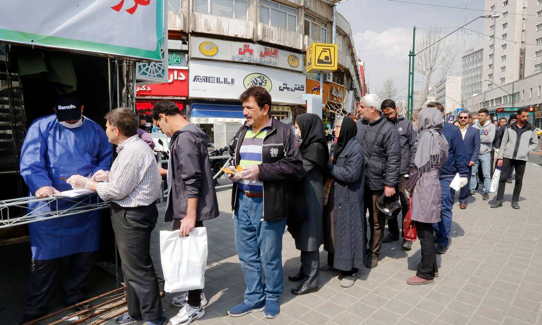 Pessoas fazem fila para receber pacotes com itens usados para tentar evitar o contágio pelo coronavírus em Teerã Foto: STRINGER / AFP