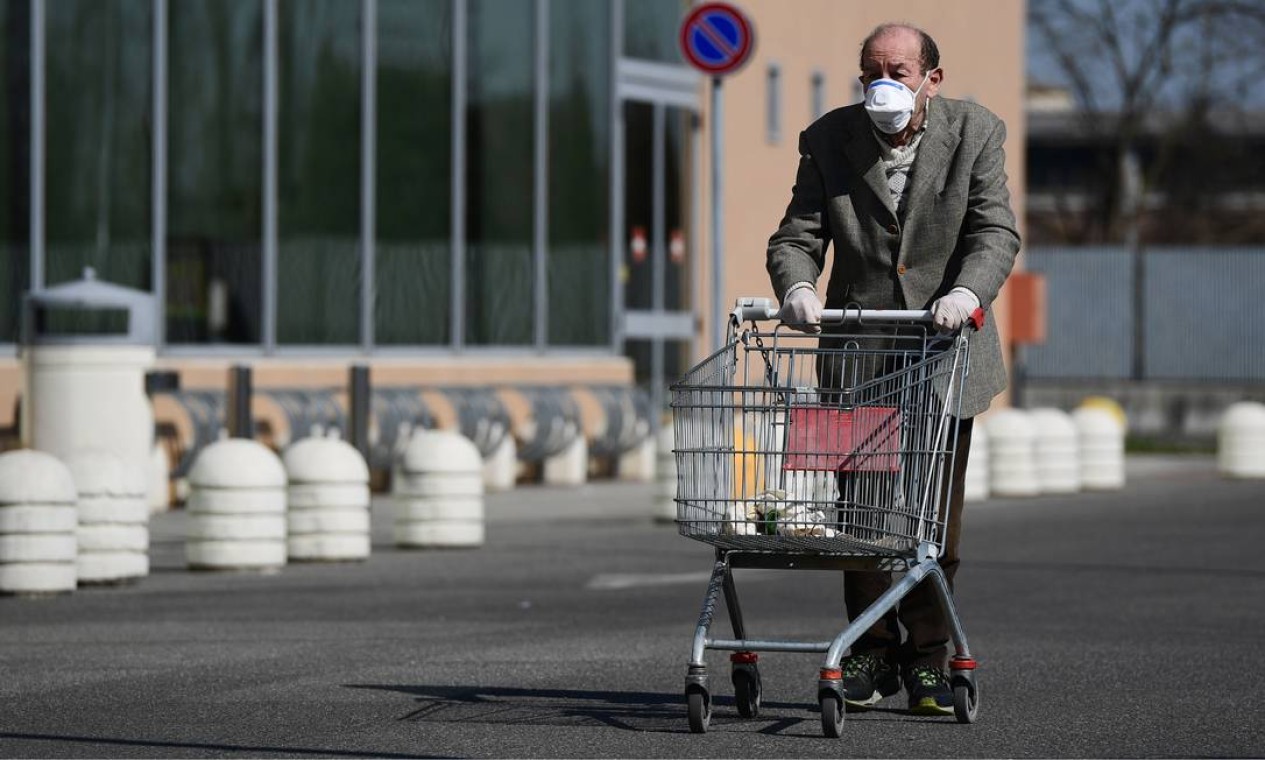 Idoso usando uma máscara protetora empurra seu carrinho quando chega para fazer compras em um supermercado em Codogno, sudeste de Milão, depois que a Itália impôs restrições nacionais aos seus 60 milhões pessoas para controlar a Covid-19. Itália é um país de idosos, o mais antigo da Europa, segundo as estatísticas, e poucos deles moram em casas de repouso, a questão de seu isolamento é aguda Foto: MIGUEL MEDINA / AFP