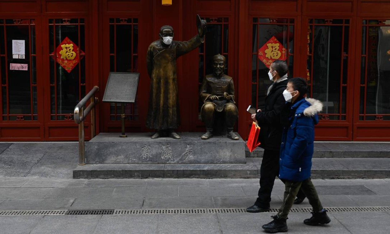 Pessoas usam máscaras enquanto passam em frente a uma estátua também com máscara em uma rua de Pequim, na China Foto: STR / AFP