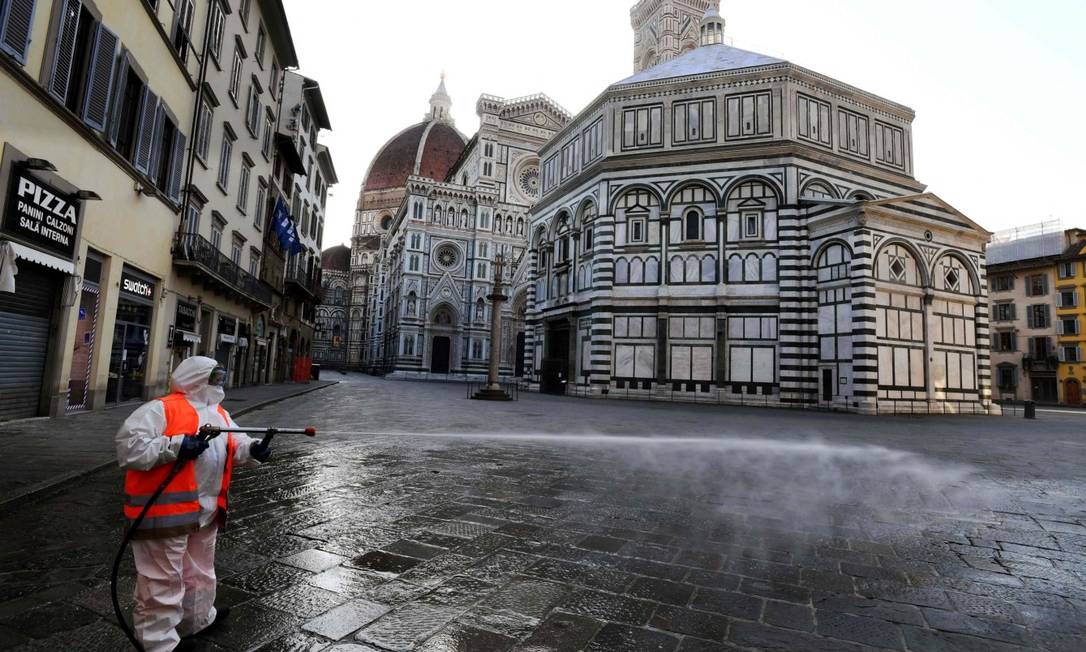 Homem desinfecta rua em Florença, na Itália, sob quarentena Foto: CARLO BRESSAN / AFP