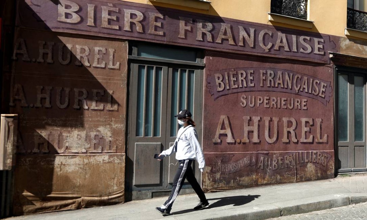 Moradora passa com máscara por rua em Paris que havia sido ambientada para reproduzir os anos 1940 para filme de época Foto: CHARLES PLATIAU / REUTERS