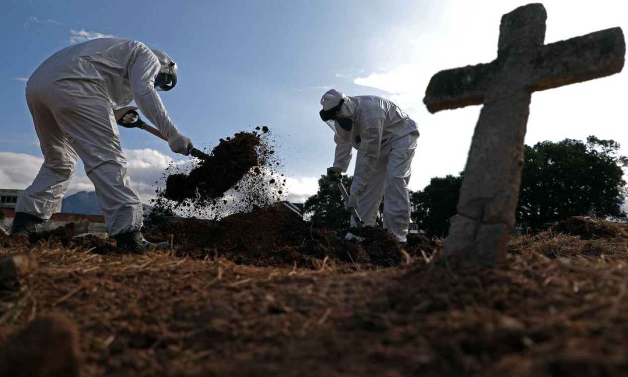 Mudanças de protocolo: funcionários usam traje de proteção enquanto fazem o enterro de uma vítima da Covid-19 em área de segurança no Cemitério do Caju Foto: FABIO MOTTA / Agência O Globo