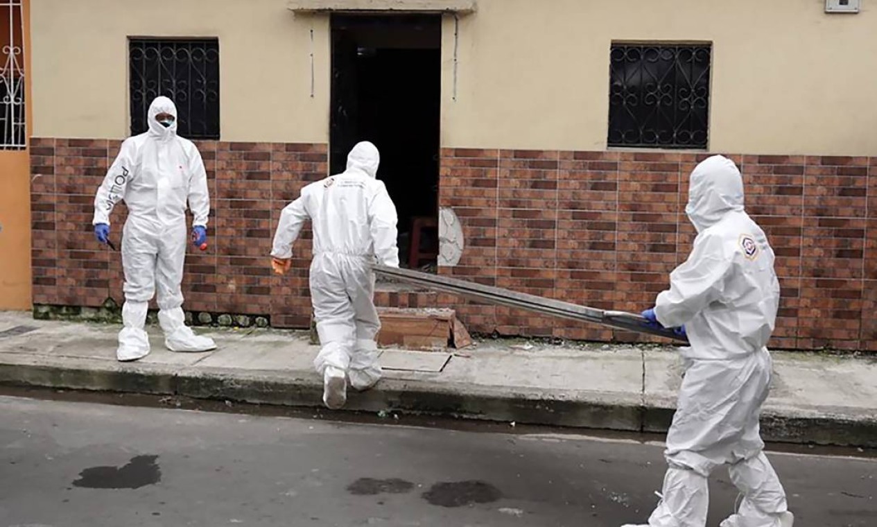 Policiais e funcionários de medicina forense se dirigem a uma casa para a retirada do corpo de uma vítima da Covid-19 em Guayaquil. A cidade portuária onde foi detectado o primeiro caso, importado da Espanha, registra 70% dos 2.758 casos de infectados no país Foto: - / AFP