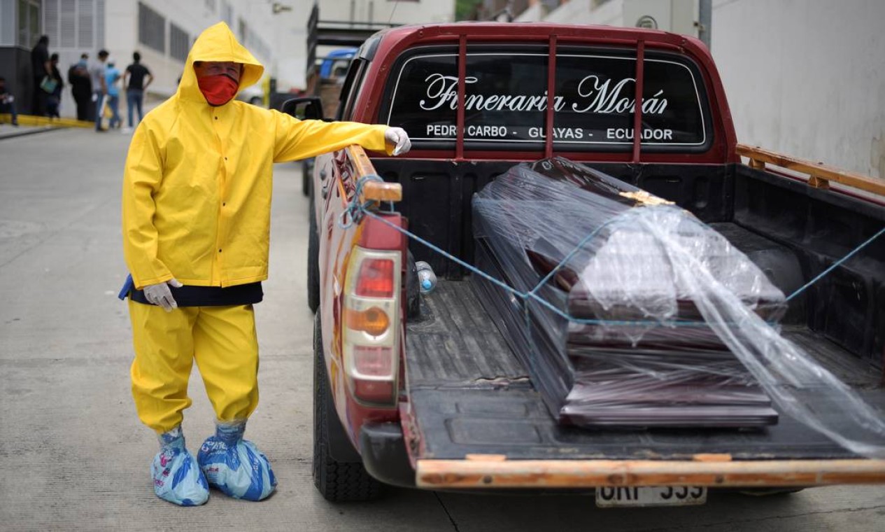 Um funcionário de uma funerária em um traje de proteção aguarda com um caixão em uma caminhonete nos arredores do hospital Los Ceibos. Apenas na quarta-feira, foram retirados 150 corpos, ainda não testados para a Covid-19 Foto: STRINGER / REUTERS
