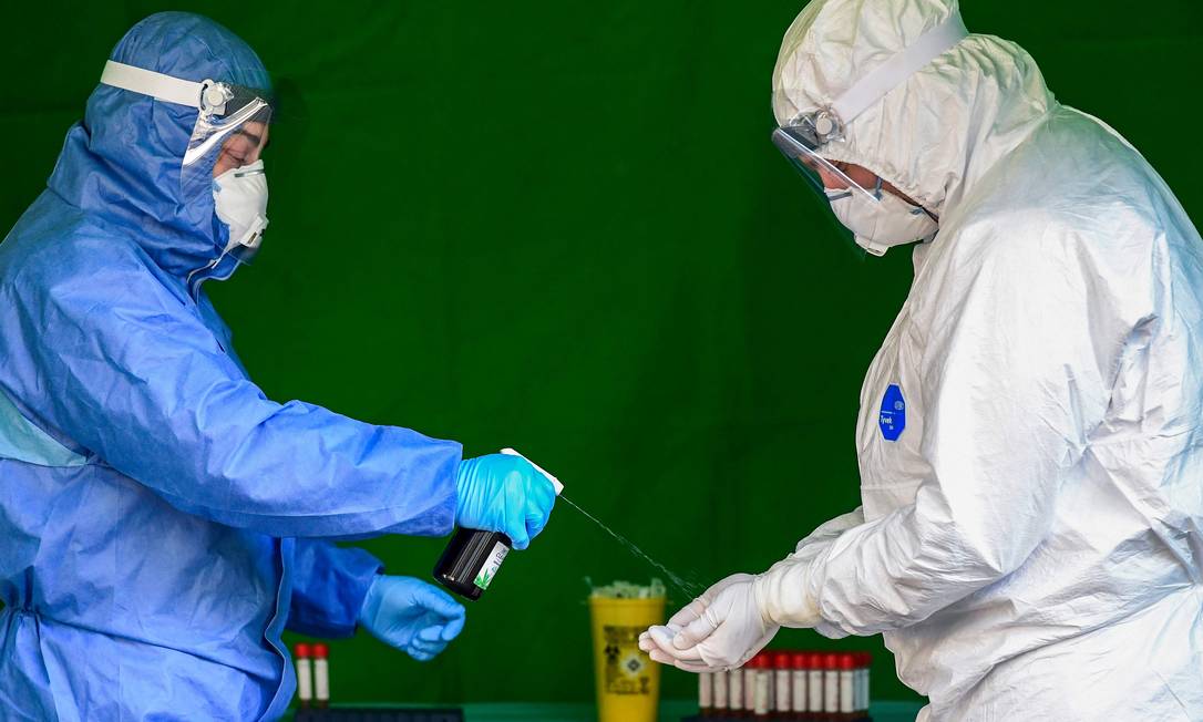 Profissionais de saúde desinfetam as luvas enquanto realizam testes para diagnosticar o coronavírus Foto: Miguel Medina / AFP