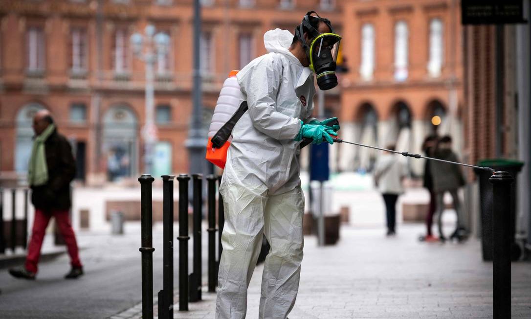 Homem com roupa de proteção desinfecta rua em Tolouse, na França Foto: LIONEL BONAVENTURE / AFP