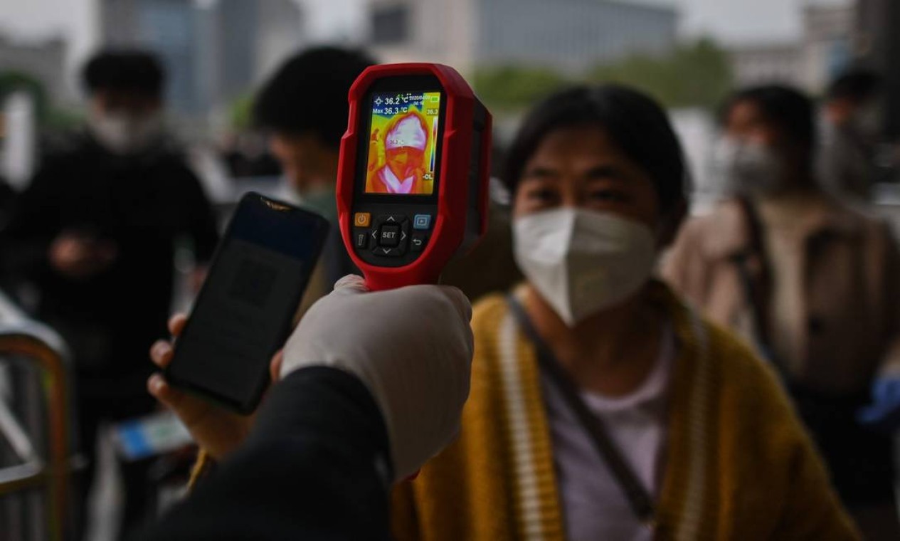 Nova rotina. Operária verifica a temperatura de passageira na Estação Ferroviária Hankou, em Wuhan, nesta quarta-feiram quando um dos primeiros trens sairam da cidade na província central de Hubei, depois de mais de dois meses sem realizar viagens Foto: HECTOR RETAMAL / AFP