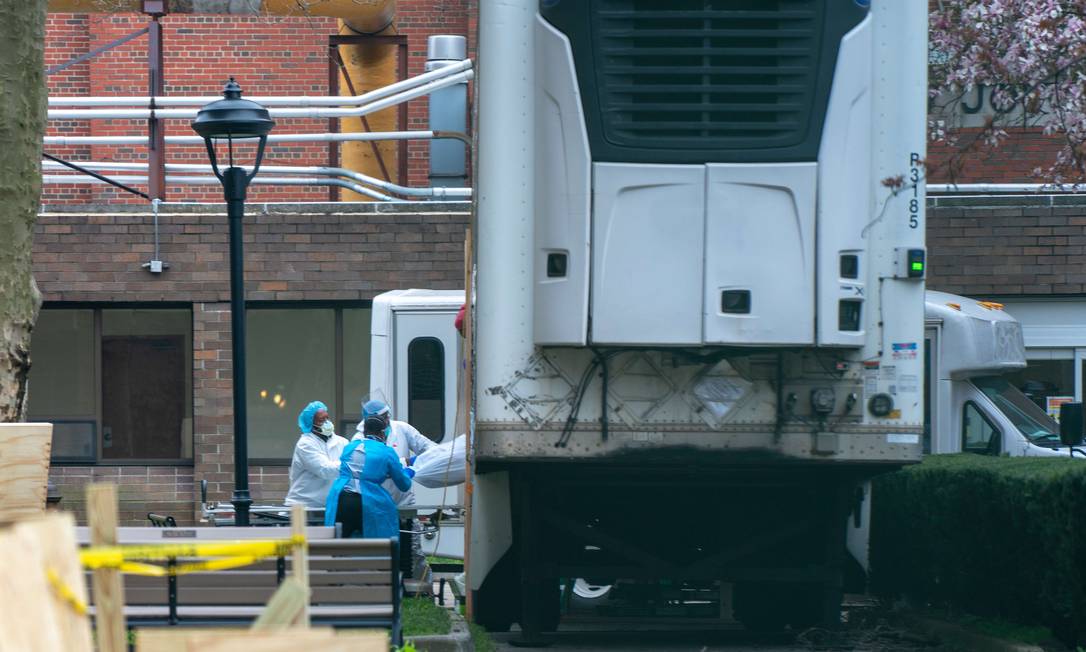 Funcionários de hospital em Nova York carregam corpo de vítima da Covid-19 para caminhão refrigerado Foto: David Dee Delgado / AFP