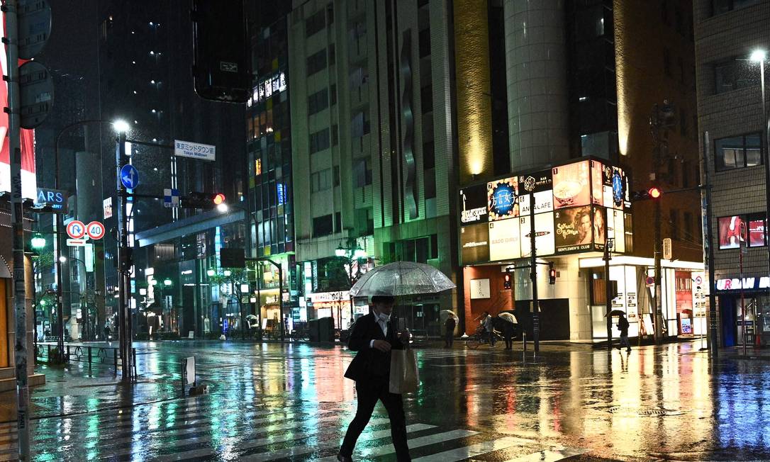 Homem usando máscara de proteção caminha com seu guarda-chuva no distrito de Roppongi, em Tóquio Foto: PHILIP FONG / AFP/09-04-2020
