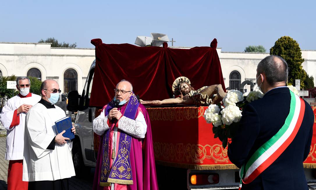 Um padre usando uma máscara reza ao lado do prefeito de Cernusco sul Naviglio, Ermanno Zacchetti, em um cemitério, em homenagem às vítimas Foto: FLAVIO LO SCALZO / REUTERS