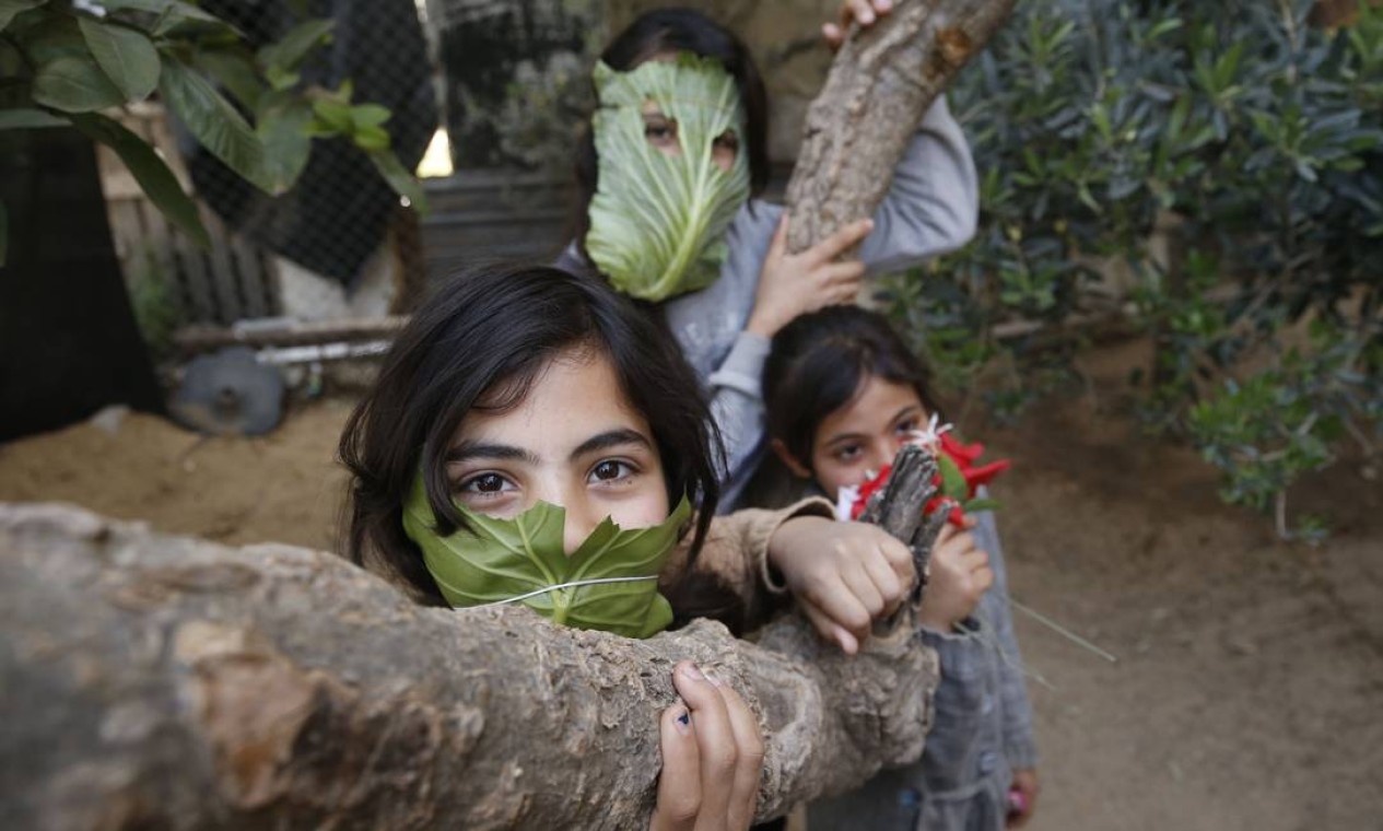 Crianças palestinas usam máscaras improvisadas feitas de folhas de repolho em Beit Lahia, no norte da Faixa de Gaza, em meio à pandemia de Covid-19. Foto: MOHAMMED ABED / AFP - 16/04/2020