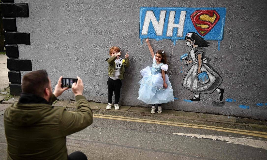Crianças posam para uma foto junto a um grafite em homenagem ao sistema público de saúde britânico em Pontefract, no norte da Inglaterra AFP Foto: Oli Scarff / AFP