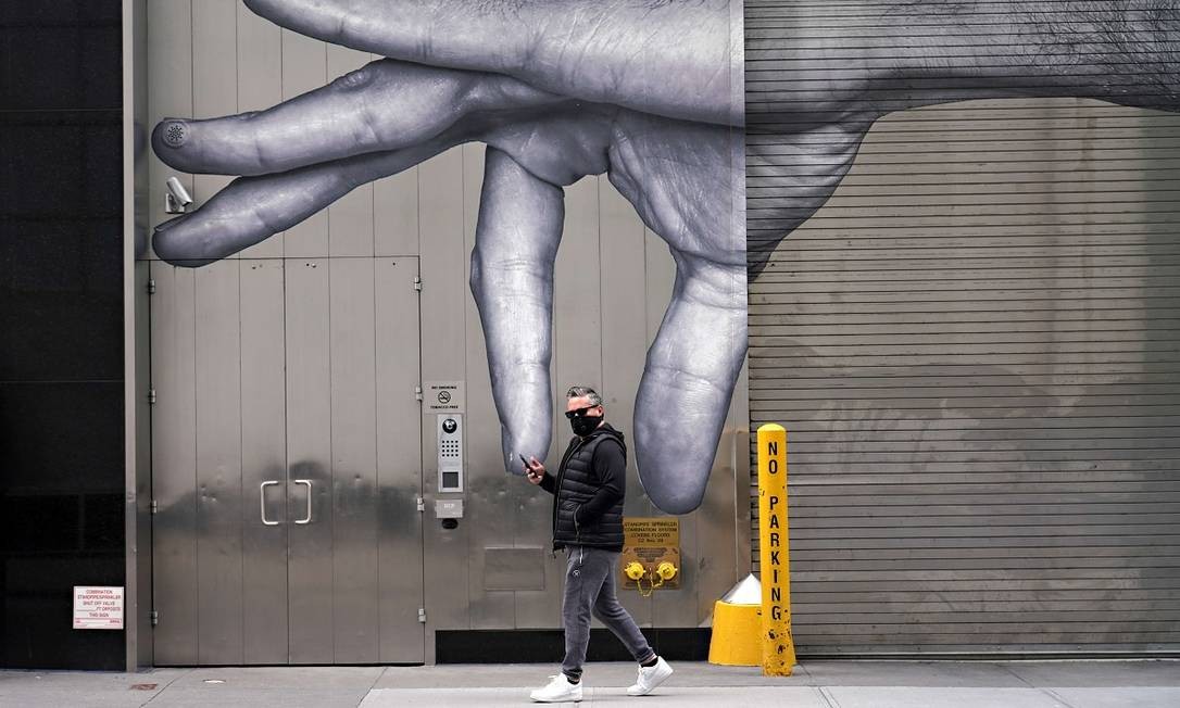 Um homem usando máscara contra o novo coronavírus passa em frente a um grafite em Nova York Foto: Cindy Ord / AFP