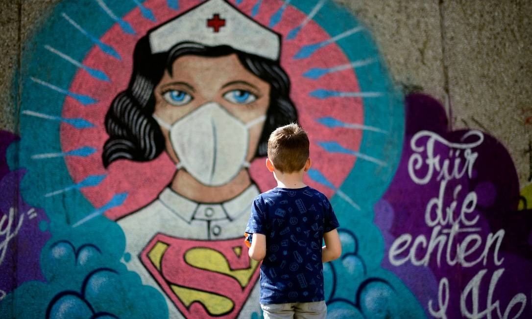 Um menino observa uma pintura mural, do artista Kai 'Uzey' Wohlgemuth, em que uma enfermeira é retratada como uma super-heroína, em Hamm, no oeste da Alemanha Foto: Ina Fassbender / AFP