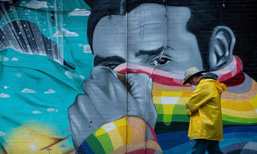 Em Nova York, um homem usando uma máscara para não se infectar com o novo coronavírus caminha em frente a um muro, onde um grafite retrata outro homem cobrindo o rosto Foto: Johannes Eisele / AFP