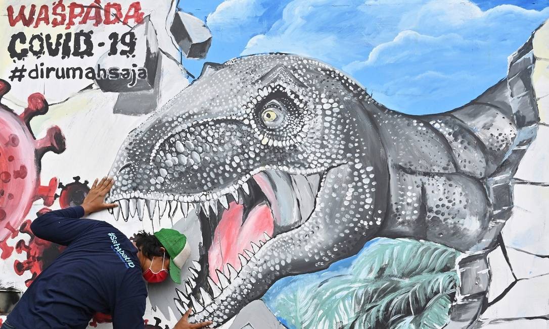 Seriam os dinossauros a solução para a pandemia? O grafiteiro Ray Andree posa junto a um animal pré-histórico que ele incluiu num mural sobre a Covid-19, em Depok, Indonésia Foto: Adek Berry / AFP