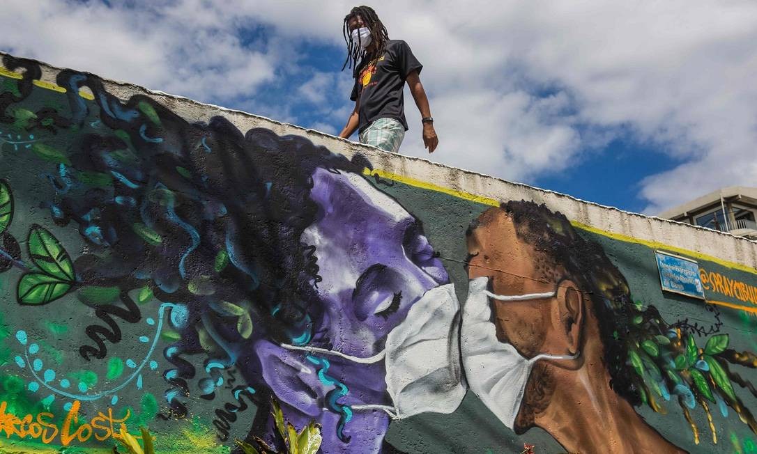 Um homem caminha acima da pintura mural do grafiteiro Marcos Costa, o Spraycabuloso, que mostra um casal usando máscara contra a Covid-19, na entrada da favela do Solar do Unhão, em Salvador Foto: Antonello Veneri / AFP