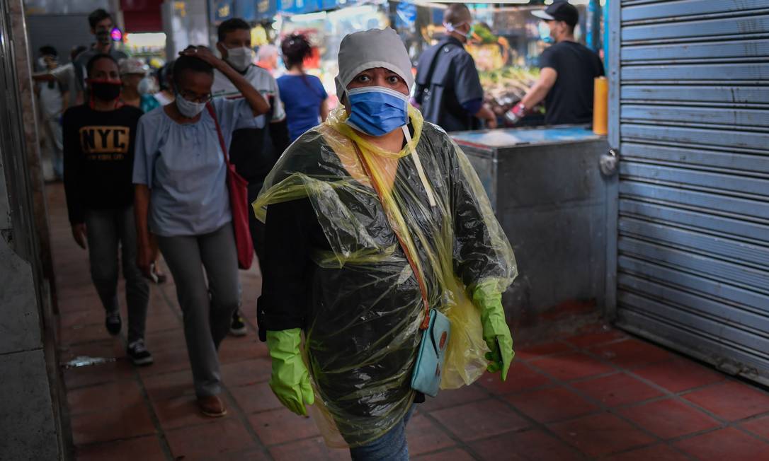 Mulher com máscara, luva e proteção caseiras caminha em mercado em Caracas Foto: FEDERICO PARRA / AFP
