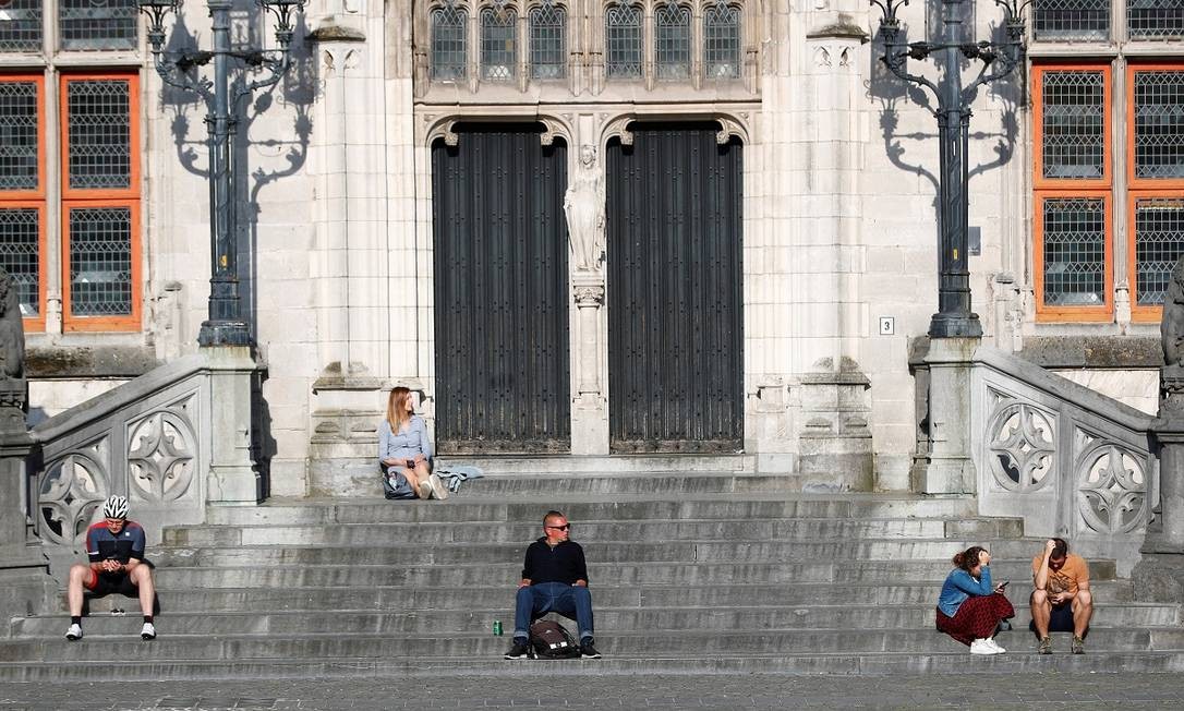 Poucas pessoas aproveitam o sol da primavera nas escadas de uma construção no centro histórico de Bruges Foto: Francois Lenoir / Reuters