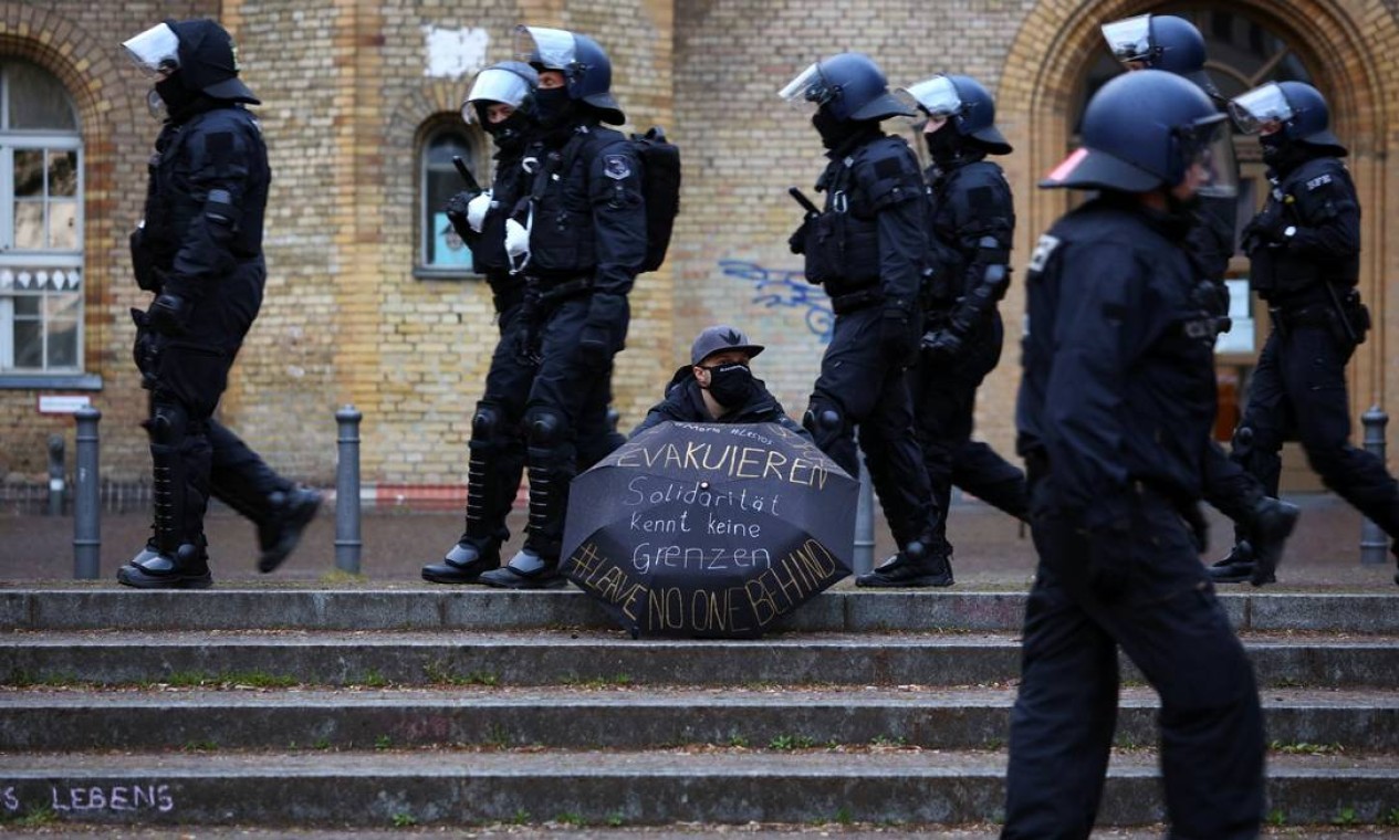 Policiais de máscara passam por um manifestante segurando um guarda-chuva com a inscrição "solidariedade não conhece fronteiras", durante uma manifestação no dia 1º de maio, em meio à disseminação do coronavírus em Berlim, na Alemanha Foto: CHRISTIAN MANG / REUTERS