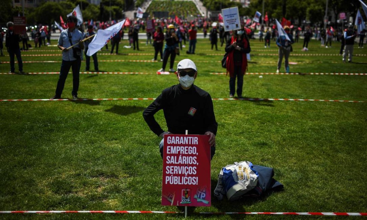 Um homem usando uma máscara facial e segurando um cartaz com a inscrição "Garantir salários, empregos, serviços públicos" participa de um ato do Dia do Trabalhador em Lisboa, Portugal Foto: PATRICIA DE MELO MOREIRA / AFP