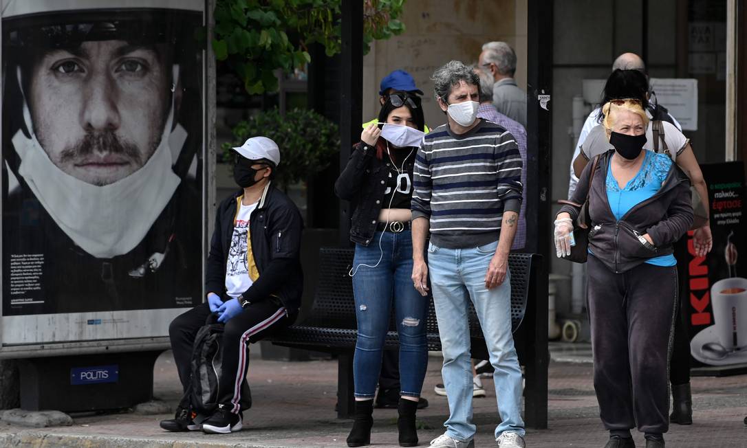 Pessoas usam máscaras em ponto de ônibus de Atenas, no primeiro dia de afrouxamento da quarentena Foto: LOUISA GOULIAMAKI / AFP