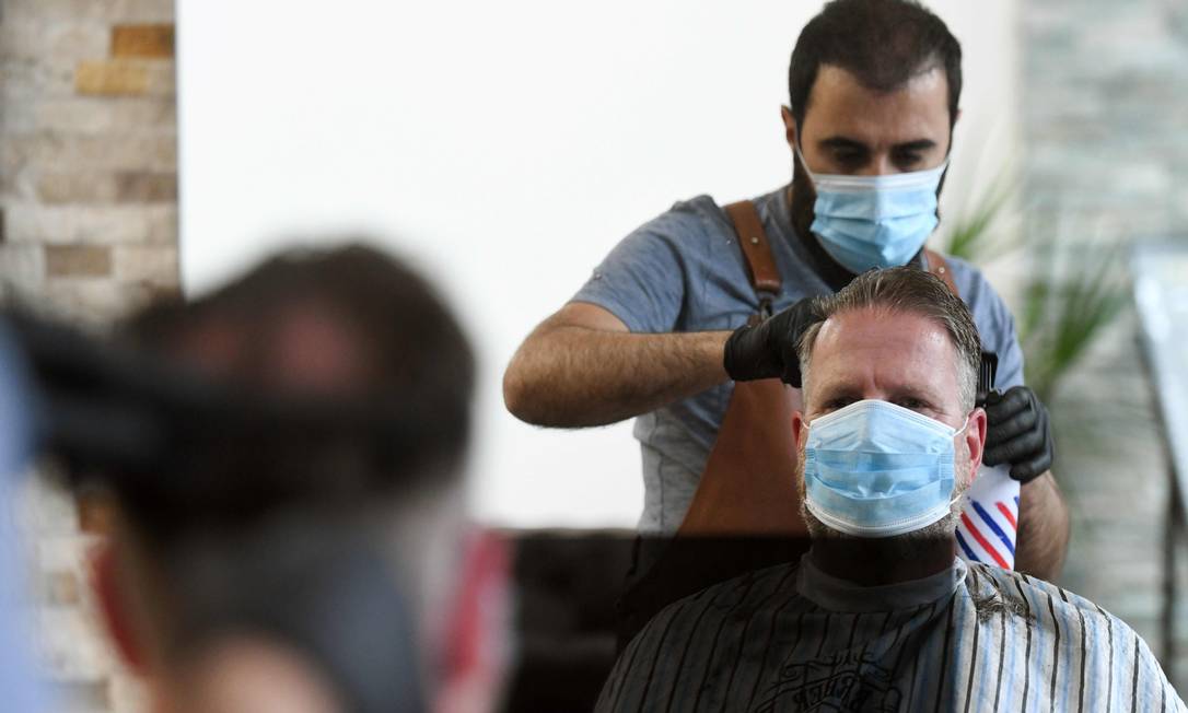 Cabeleireiro usa máscara para cortar cabelo de cliente na Alemanha, onde parte do comércio pode voltar a funcionar Foto: INA FASSBENDER / AFP