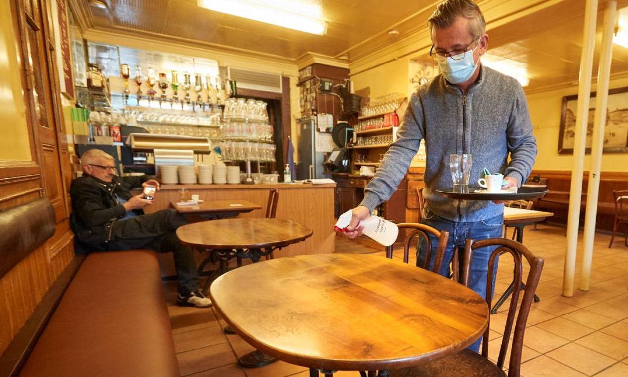 Garçom desinfeta mesa depois de cliente deixá-la no Cafe du Soleil, em Genebra, na Suíça, que também começou a flexiblizar as regras do lockdown Foto: DENIS BALIBOUSE / REUTERS