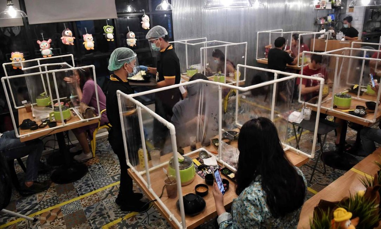 Clientes comem entre as divisórias plásticas, criadas para conter qualquer disseminação do coronavírus no restaurante Penguin Eat Shabu, em Bangkok Foto: LILLIAN SUWANRUMPHA / AFP