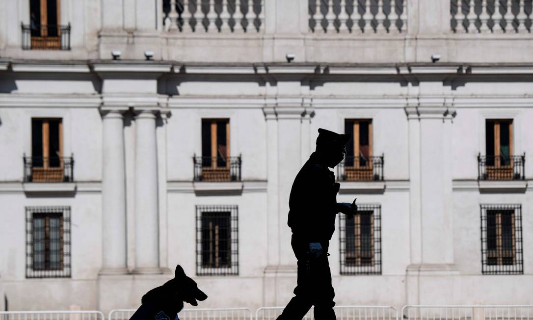 Um policial e seu cachorro caminham do lado de fora do palácio presidencial do Chile, em Santiago, no dia em que o governo anunciou um confinamento total na capital Foto: Martin Bernetti / AFP