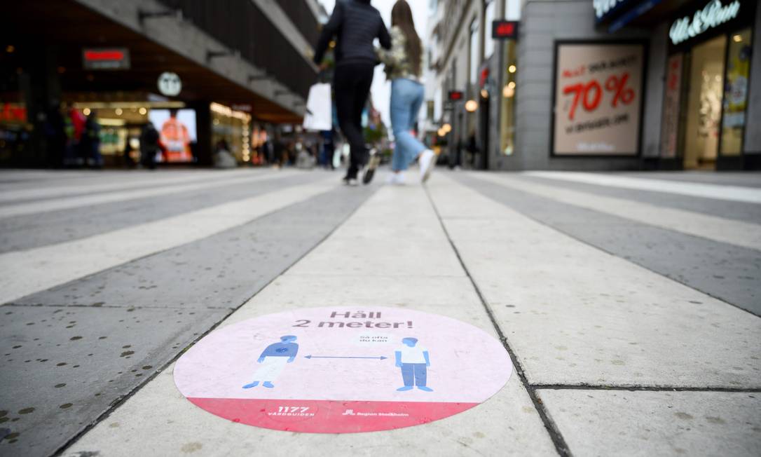 Adesivo em rua comercial de Estocolmo pede que as pessoas mantenham distância de pelo menos dois metros em relação a outros transeuntes Foto: HENRIK MONTGOMERY / AFP