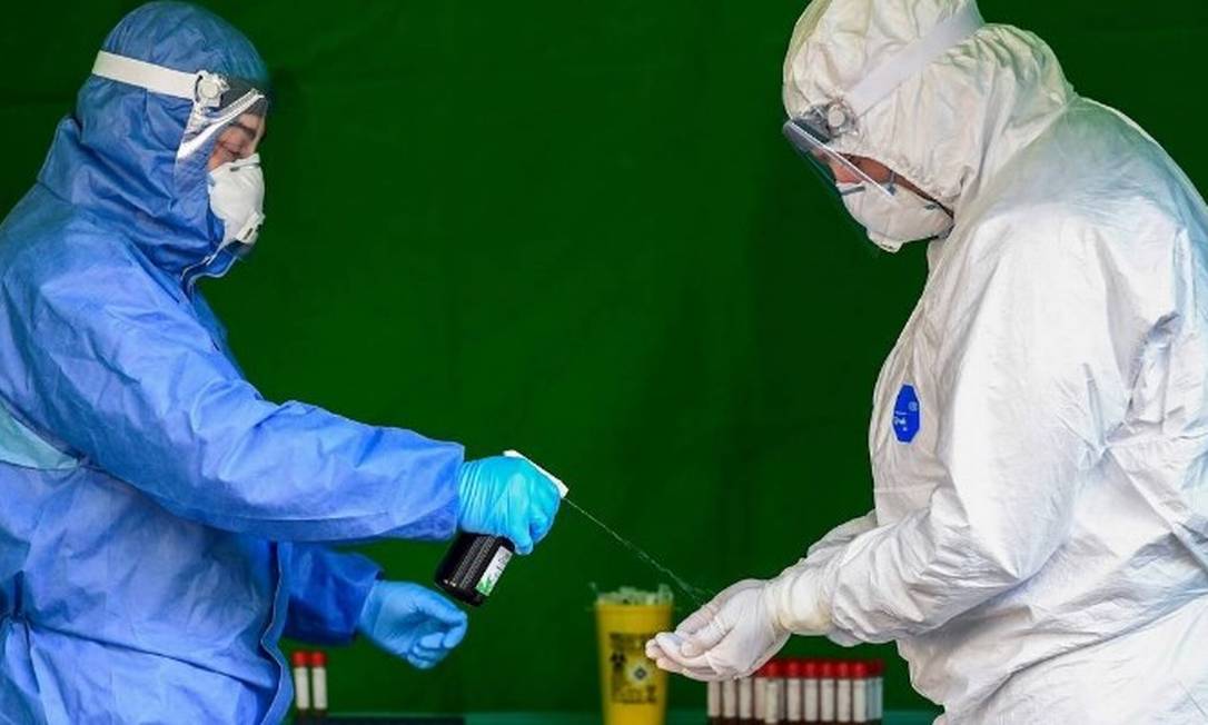 Profissionais de saúde desinfetam as luvas enquanto realizam testes para diagnosticar o coronavírus Foto: MIGUEL MEDINA/AFP