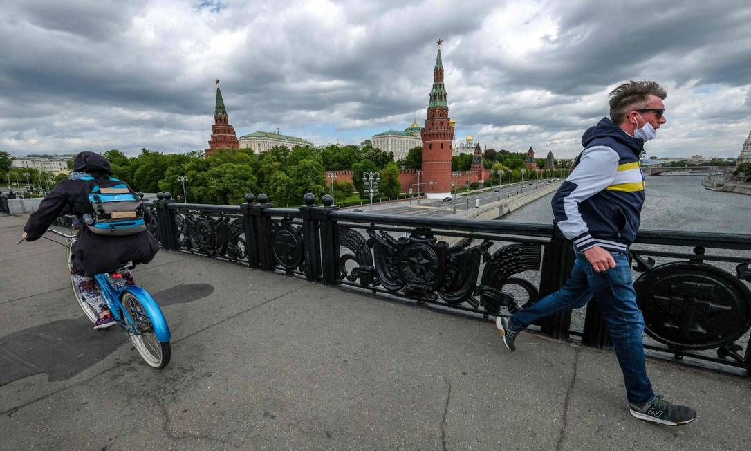 Homem com a máscara, usada incorretamente, percorre a ponte em frente ao Kremlin, em Moscou Foto: YURI KADOBNOV / AFP