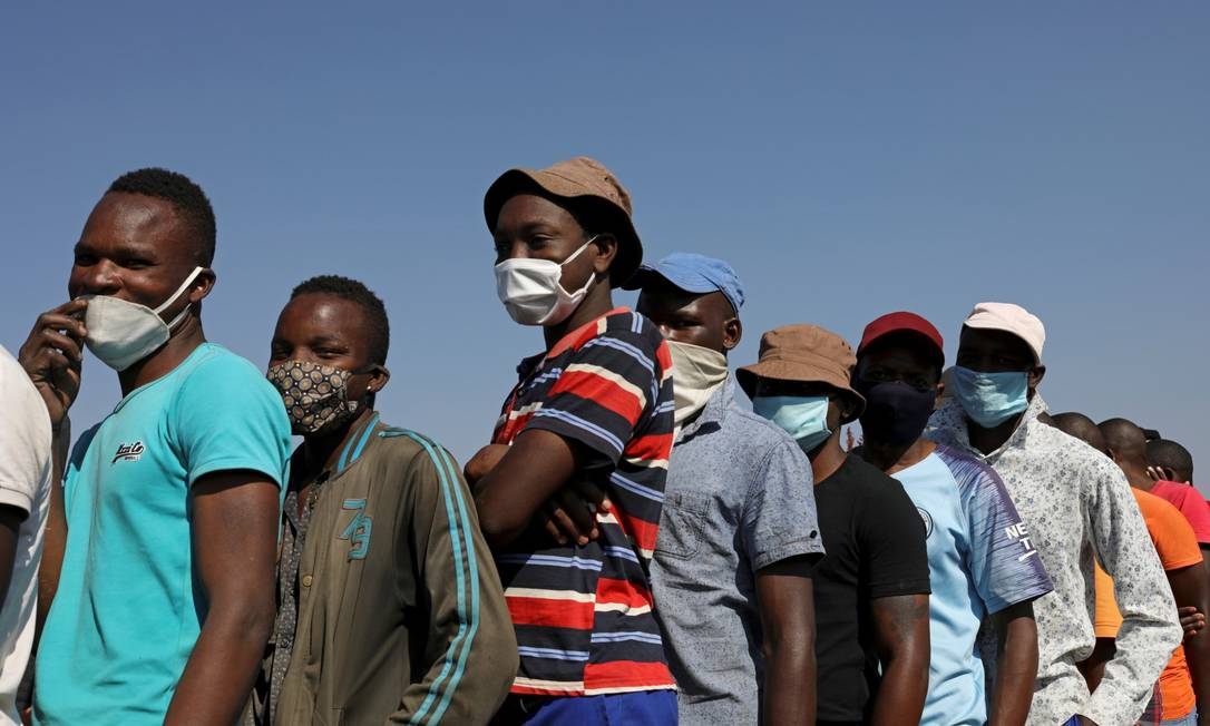 Na África do Sul, pessoas de máscara esperam para receber comida Foto: Siphiwe Sibeko / REUTERS
