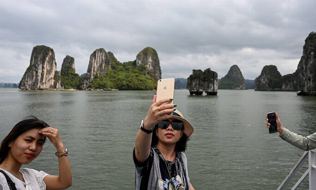 Turistas vietnamitas tiram selfies durante um passeio de barco na Baía de Ha Long, no Vietnã Foto: Manan Vatsyayana / AFP