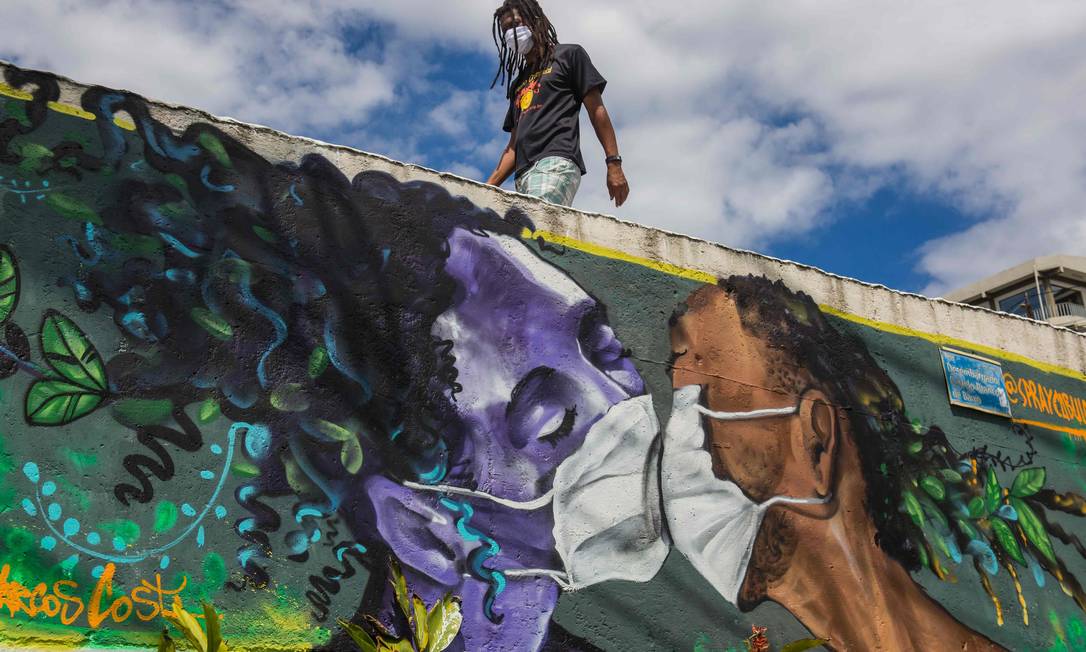 Um homem usando uma máscara facial passa por um grafite do artista Marcos Costa na entrada da favela Solar de Unhao, em Salvador. Foto: ANTONELLO VENERI / AFP