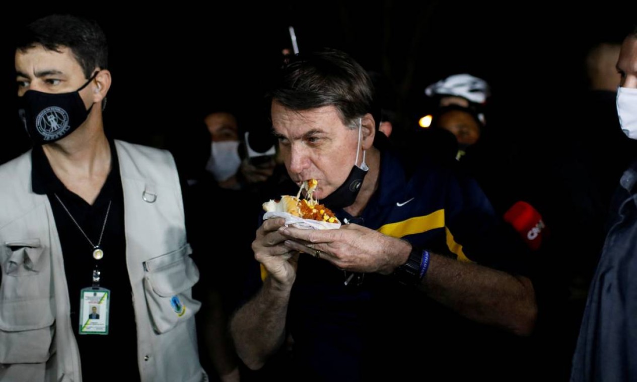 O presidente Jair Bolsonaro come um cachorro-quente em uma lanchonete de rua, em meio ao surto de coronavírus, em Brasília, gerando aglomeração com sua presença Foto: ADRIANO MACHADO / REUTERS