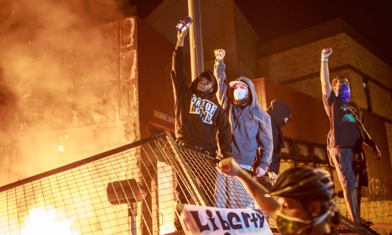 Manifestantes erguem punho cerrado as chamas se espalham pela frente da Terceira Delegacia de Polícia, na noite de quinta-feira Foto: KEREM YUCEL / AFP
