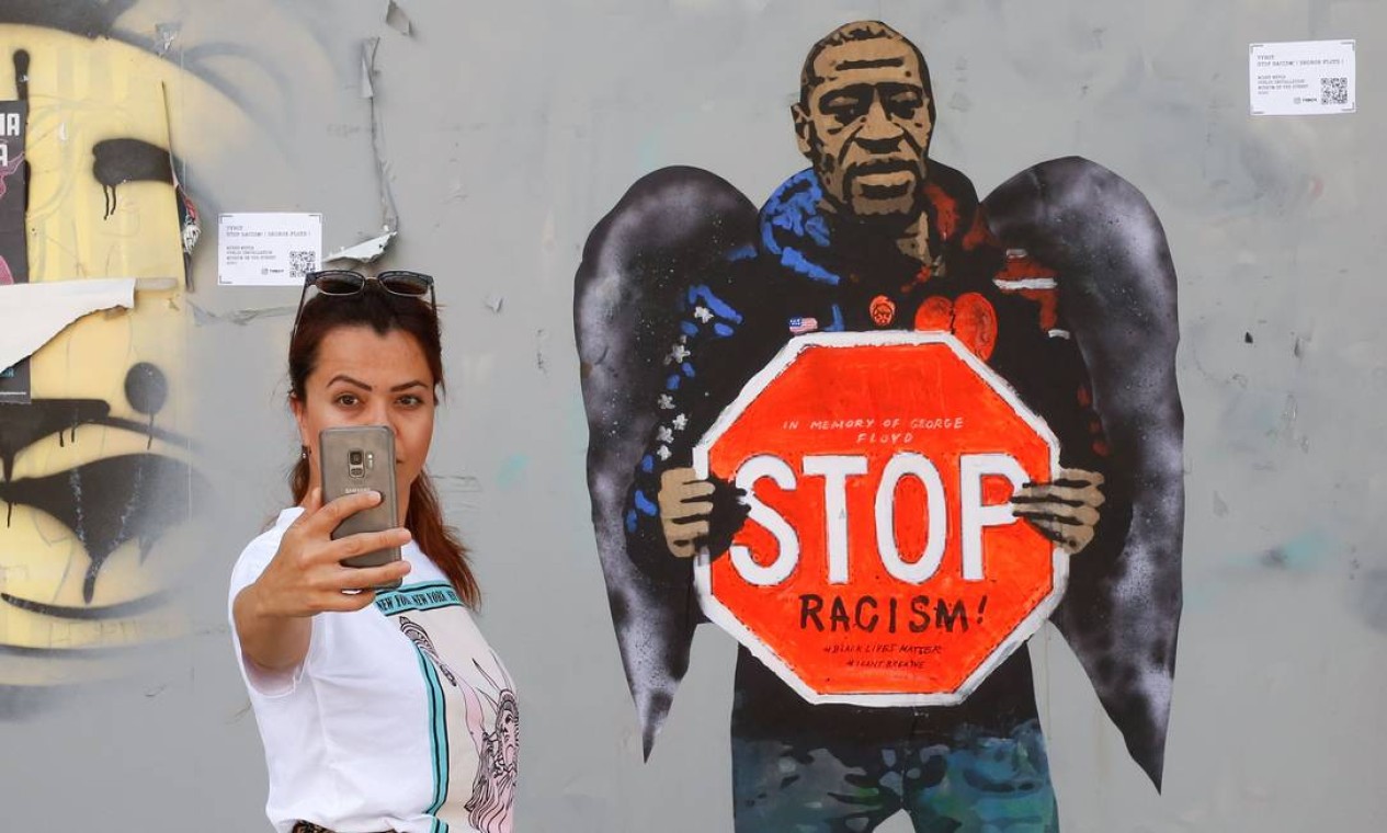 Uma mulher faz uma selfie ao lado de um grafite representando George Floyd com asas de anjo e segurando uma placa de trânsito contra o racismo, em Barcelona Foto: PAU BARRENA / AFP - 31/05/2020