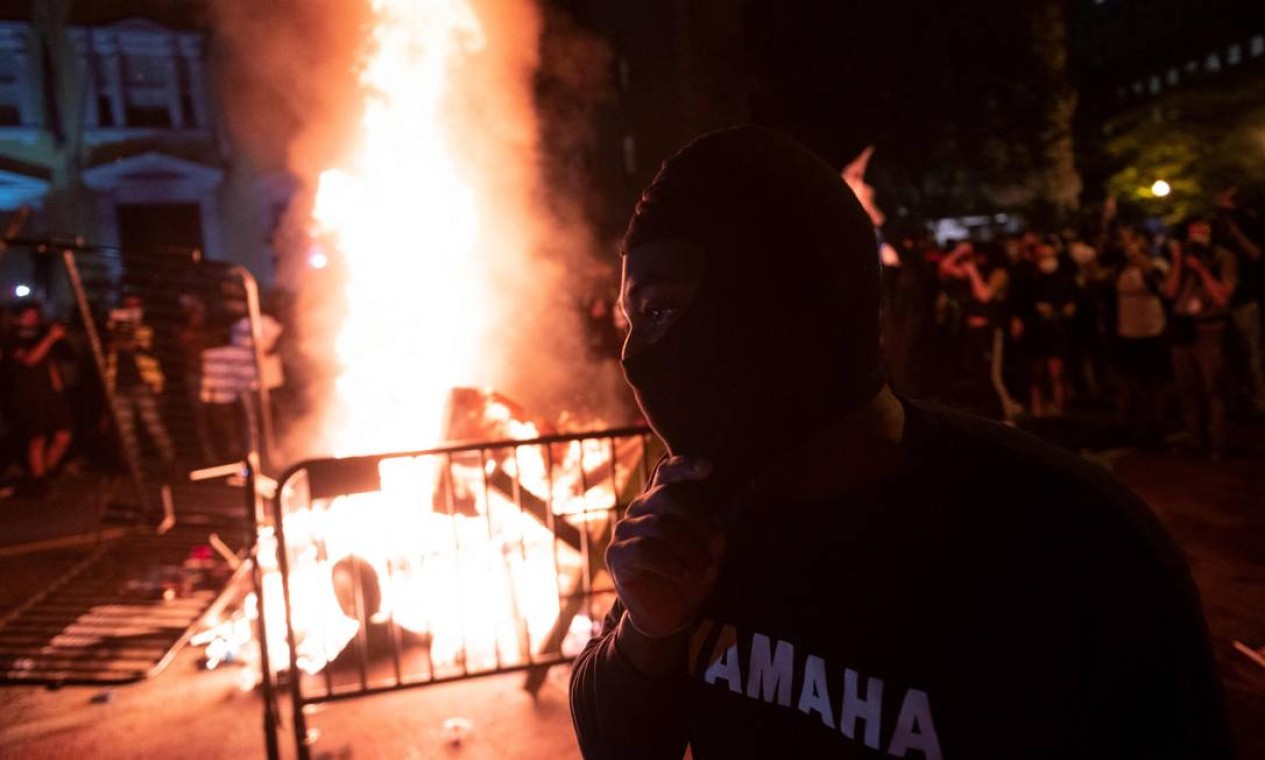 Manifestante mascarado aparece diante de fogueira feita em protesto próximo a Casa Branca, na noite de domingo Foto: ROBERTO SCHMIDT / AFP