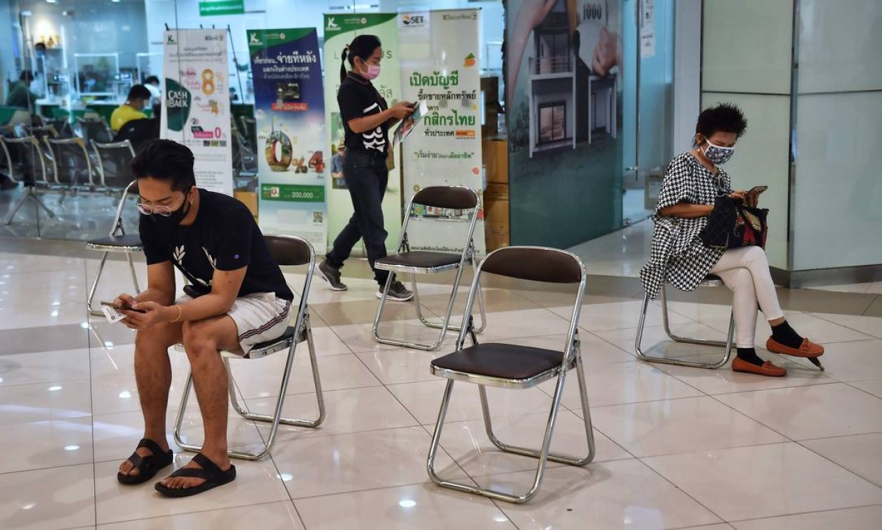 Pessoas esperam para entrar em um banco mantendo a distância social como medida preventiva contra o coronavírus, em um shopping em Bangkok Foto: LILLIAN SUWANRUMPHA / AFP