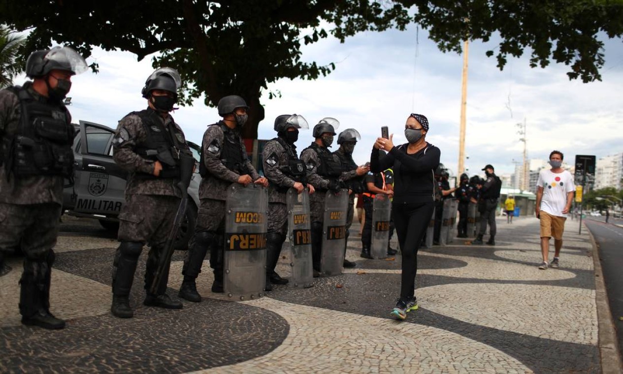 Uma mulher usando uma máscara protetora passa pela polícia de choque durante uma manifestação contra o presidente Jair Bolsonaro e em apoio à democracia na praia de Copacabana, no Rio Foto: PILAR OLIVARES / REUTERS