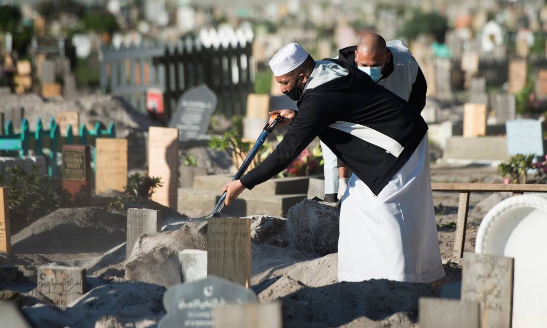 Dois homens fecham cova após funeral de um homem por coronavírus no cemitério Klip Road em Grassy Park, na Cidade do Cabo Foto: RODGER BOSCH / AFP