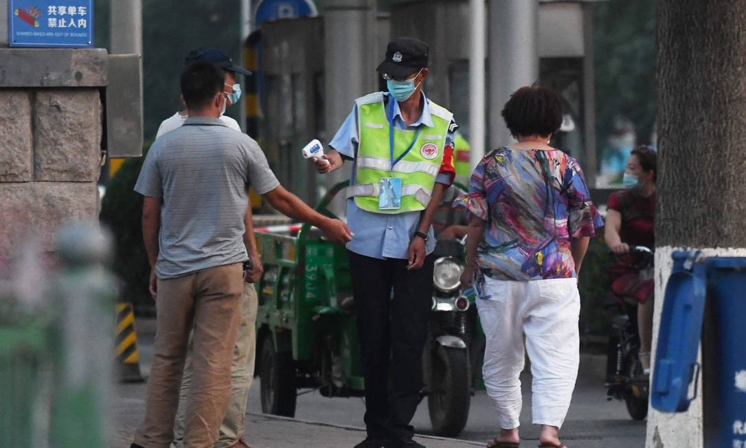 Funcionária mede a temperatura de pessoas em frente ao mercado de Xinfadi, em Pequim, um dos estabelecimentos fechados nesta sexta-feira Foto: GREG BAKER / AFP